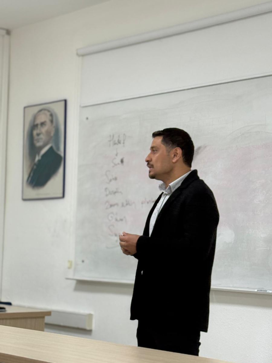 This photo captures a moment from the award ceremony. While one person is receiving an award, another person is writing on the whiteboard. At the top of the wall, there is a portrait of Atatürk. The setting appears to be an educational environment aimed at students.